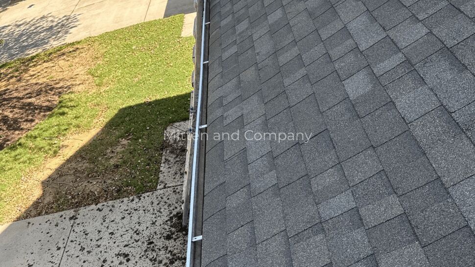Shingle Roof Gutter Edge | Mitten & Company Dark shingle roof with gutter edge above a concrete patio and lawn