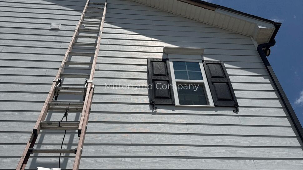 Ladder positioned against white house siding beneath a window.
