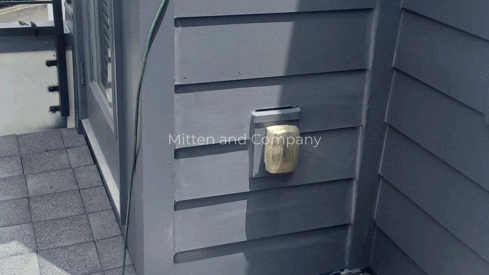 Exterior Siding Detail at Roof Corner | Mitten & Company Close-up of exterior electrical outlet mounted on gray horizontal siding at corner.