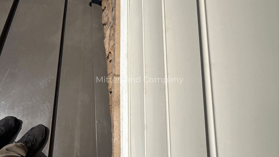 Siding and Roof Wall Junction | Mitten & Company Close view of white siding beside a dark roof edge and stone wall
