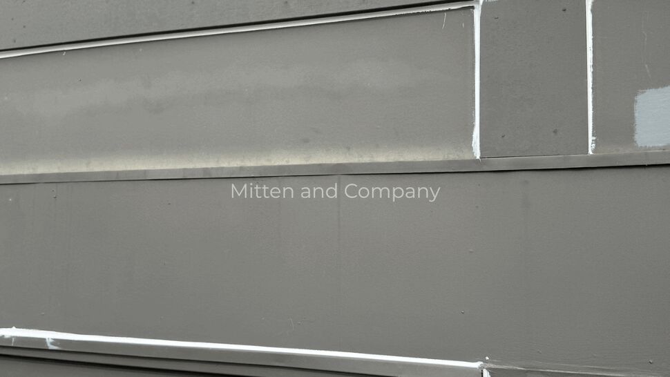 Siding trim caulking detail | Mitten & Company Close-up of gray siding panels with white caulking at the seams above a door.