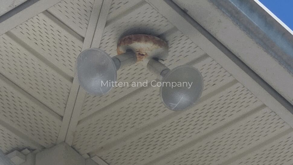 Rusted dual floodlight attached to perforated soffit near gutter
