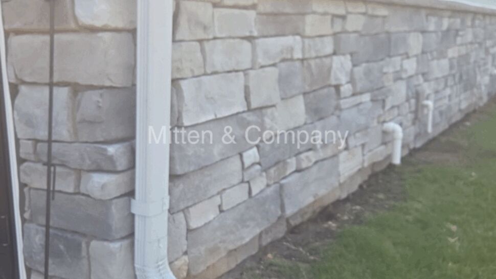 Stone veneer foundation with white downspout and green splash block