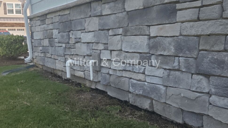Long stone veneer wall with small PVC drains and downspout