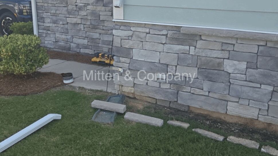 Worksite with stone veneer wall and removed downspout pieces on grass