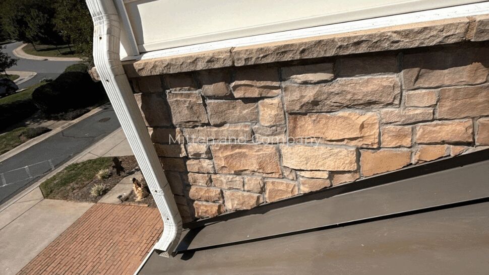 Stone Wall Roof and Downspout | Mitten & Company Stone veneer wall beside a dark metal roof and white downspout