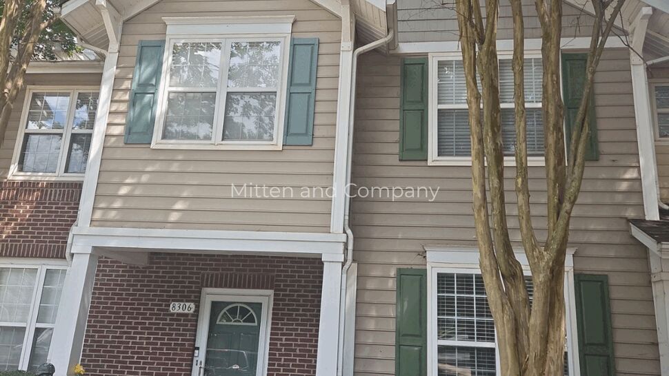 Two-story townhouse with beige siding, green shutters, brick porch, and entry door