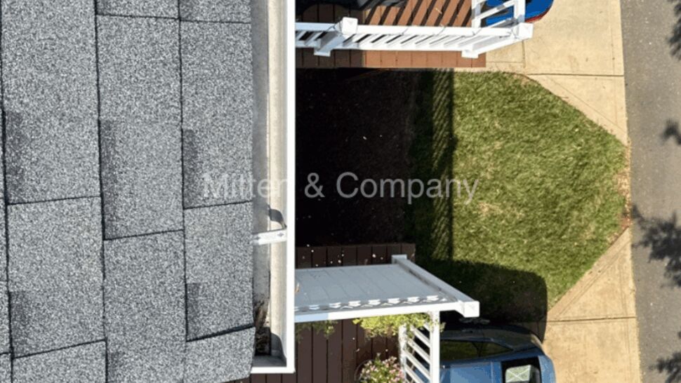Top-down view of townhouse roof, gutter, deck with grill and parked car.