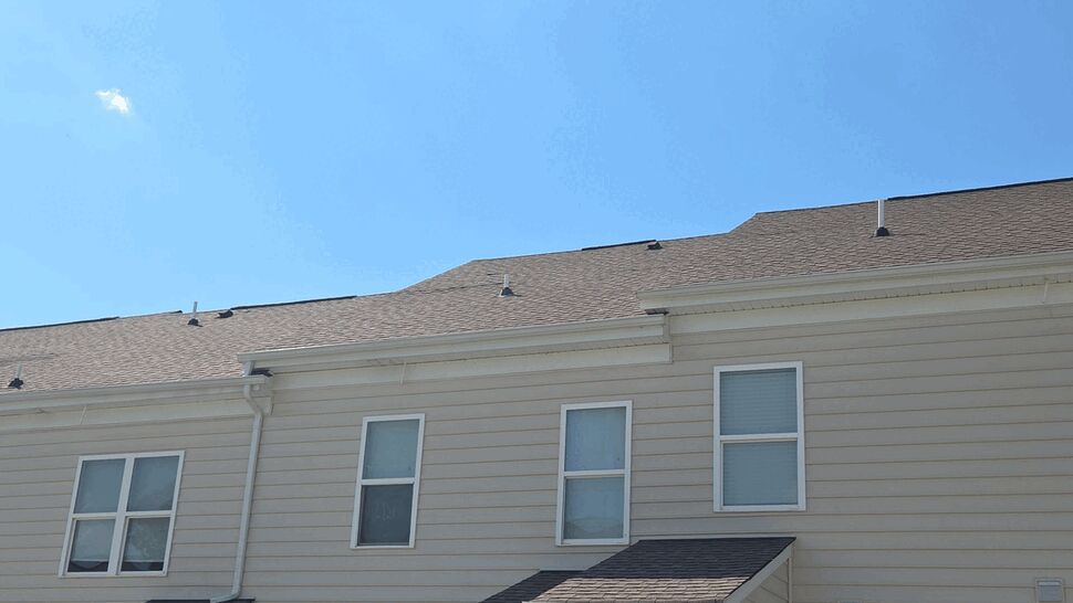Row of beige townhomes showing siding, gutters, windows, and roofline under a blue sky