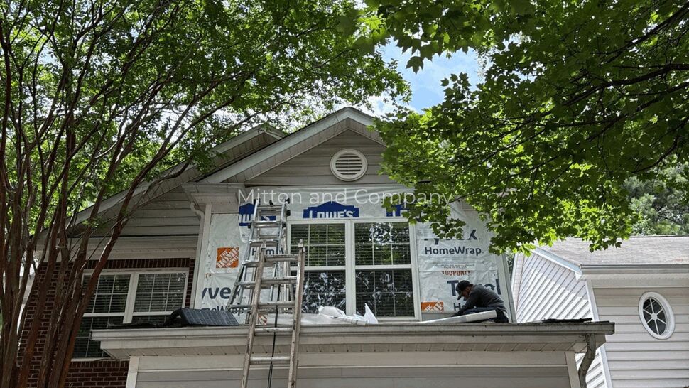 Two-Story Roof Repair with Ladder | Mitten & Company Worker on second-story roof with ladder and leafy trees overhead
