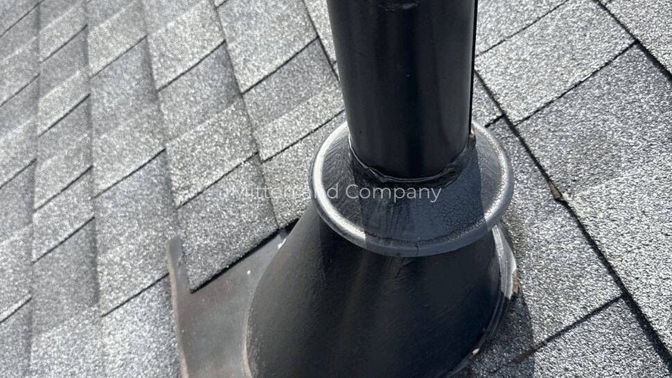 Angle view of a black vent pipe with sealed flashing on a shingle roof.