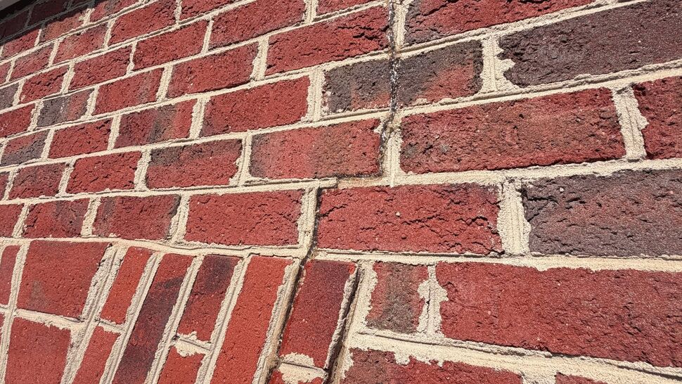 Vertical brick crack above window | Mitten & Company Red brick wall with a vertical crack above a window and separated mortar.