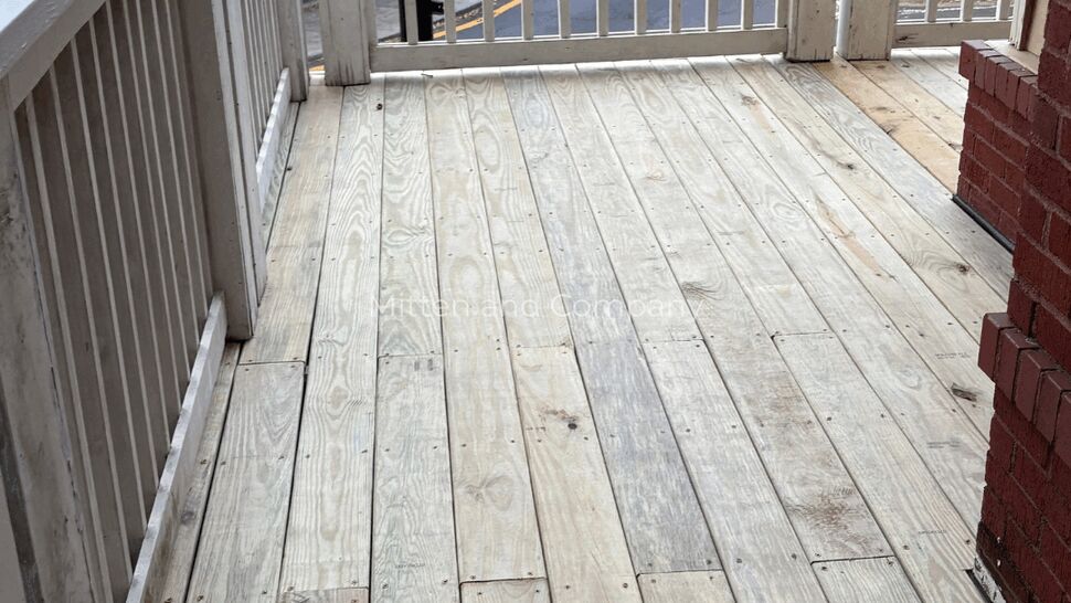 Wide Wood Porch Deck | Mitten & Company Wide view of a wood porch deck with white railings and brick walls