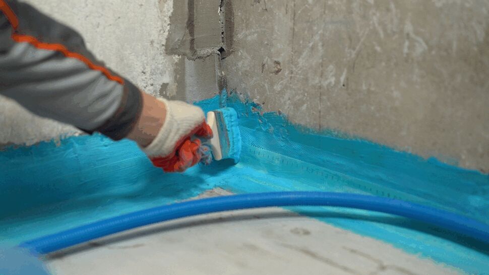 Applying blue waterproof corner seal at basement floor-wall joint