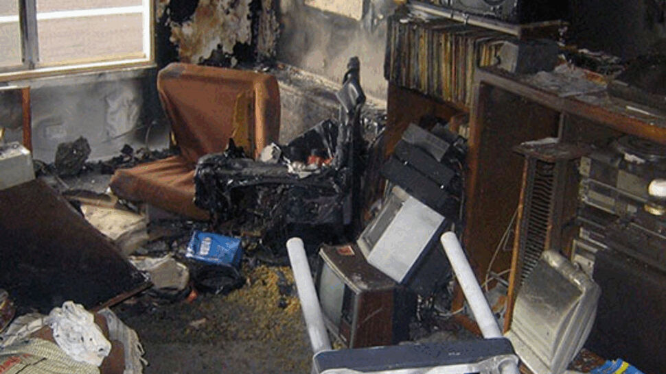 Severely fire-damaged living room with charred furniture, soot, and ruined belongings.