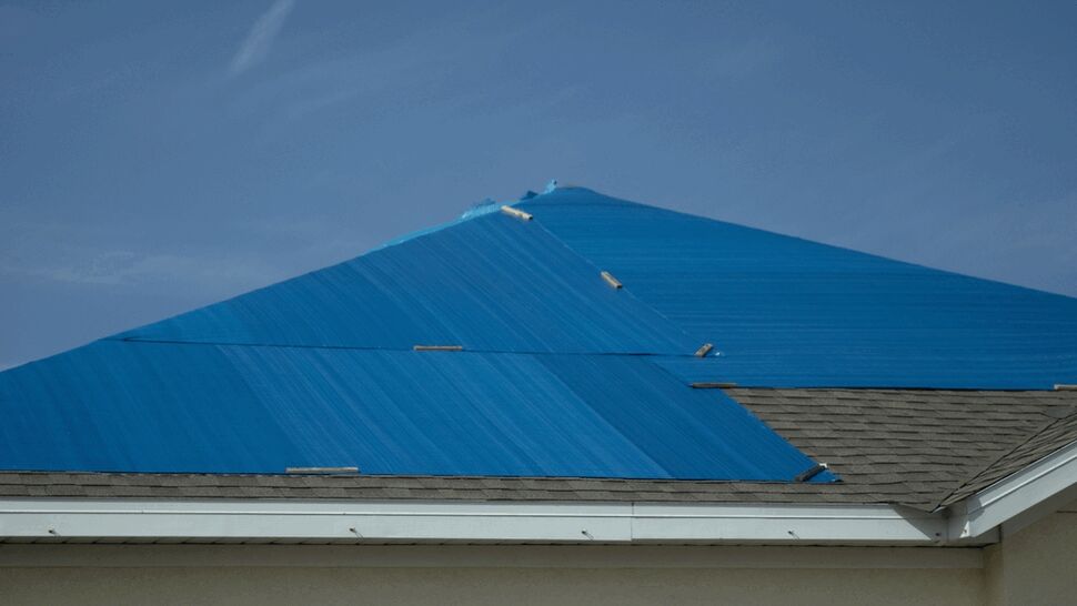 Close side view of a roof peak covered by a blue tarp secured with braces.