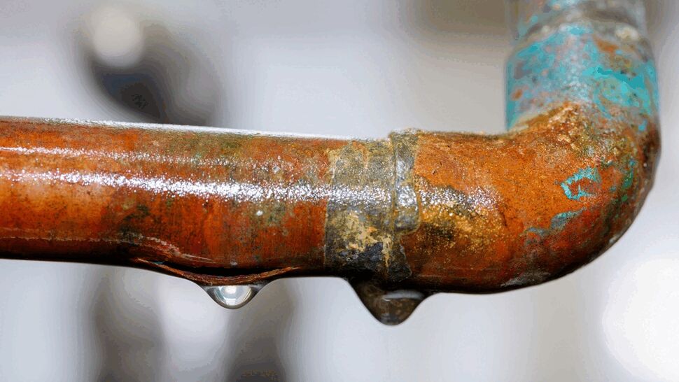 Close-up of a corroded copper elbow with a droplet forming and surface rust.