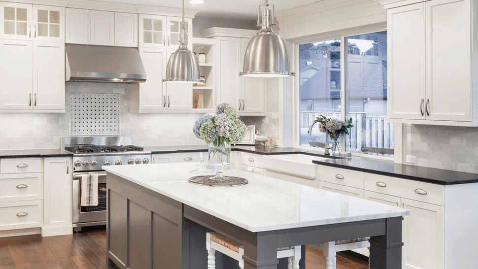 Open white kitchen with large marble island, pendant lights, and wood floor