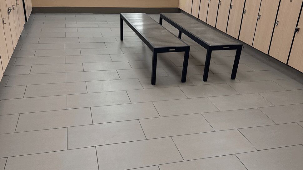 Locker room with beige large-format tile floor, wooden lockers and bench seating