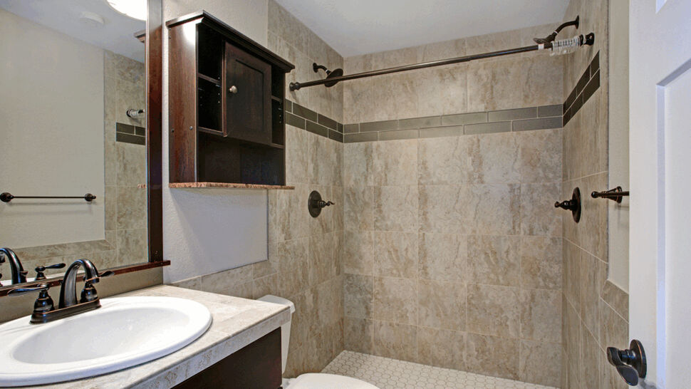 Tiled shower with decorative border and dark fixtures by a vanity
