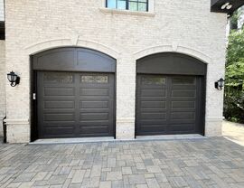Two arched dark garage doors with brick facade and paver driveway