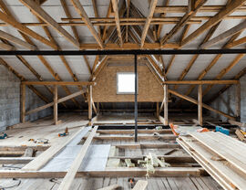 Attic interior with exposed roof trusses and partially installed subfloor during restoration.