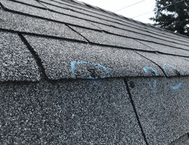 Angled roof with blue chalk marks highlighting multiple shingle issues