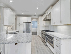 Modern white kitchen with large island, granite counters, and stainless steel appliances.