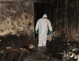 Technician in protective suit inspecting a fire-damaged room for restoration work