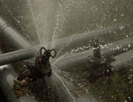 Outdoor metal pipes with a valve spraying water from a burst connection.