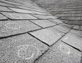 Gray asphalt shingles with chalk circles marking hail impacts