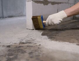 Worker brushing concrete floor sealer near concrete block wall