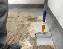 Worker rolling gray epoxy floor coating along basement edge