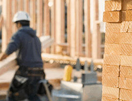 Construction worker at a framed house site with stacked lumber.