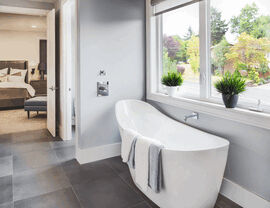 Freestanding soaking tub beside large window with towels and plants