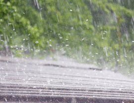 Heavy rain falling on a roof with blurred trees in the background