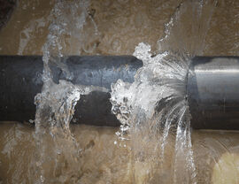Close-up of a ruptured pipe with water gushing into muddy surroundings.