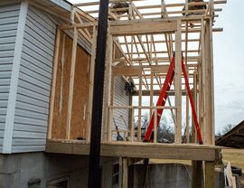 Framing for a house addition and porch with a red ladder and existing vinyl siding.