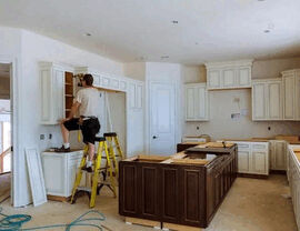 Kitchen renovation in progress with cabinets being installed and a dark island in center.