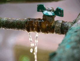 Rusty outdoor valve with a green handle slowly dripping water.