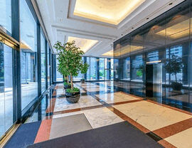 Bright marble commercial lobby with elevator, planters, and large windows.