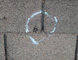 Close-up of asphalt shingle with chalk circle marking a crack