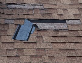 Close-up of torn and missing asphalt shingles on a brown roof.