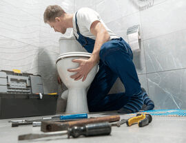 Technician kneeling installing a toilet with tools on the floor