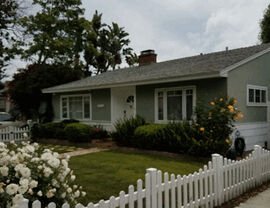 Green single-story ranch house with white picket fence and landscaped front yard.