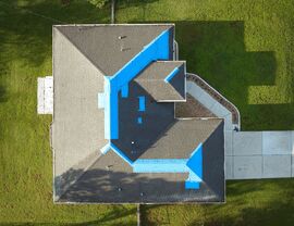 Overhead view of a home with blue tarp patches covering damaged roof areas.