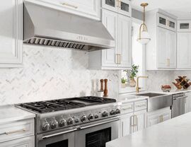 Stainless range and hood with marble herringbone backsplash and white cabinets