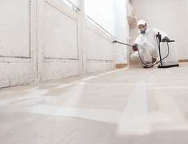 Technician in protective suit spraying treatment along a baseboard