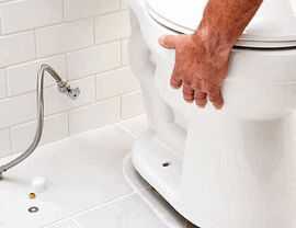 Worker positioning a toilet bowl during bathroom installation on tiled floor