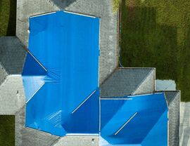 Top-down drone shot of multiple roof sections covered by blue tarps.
